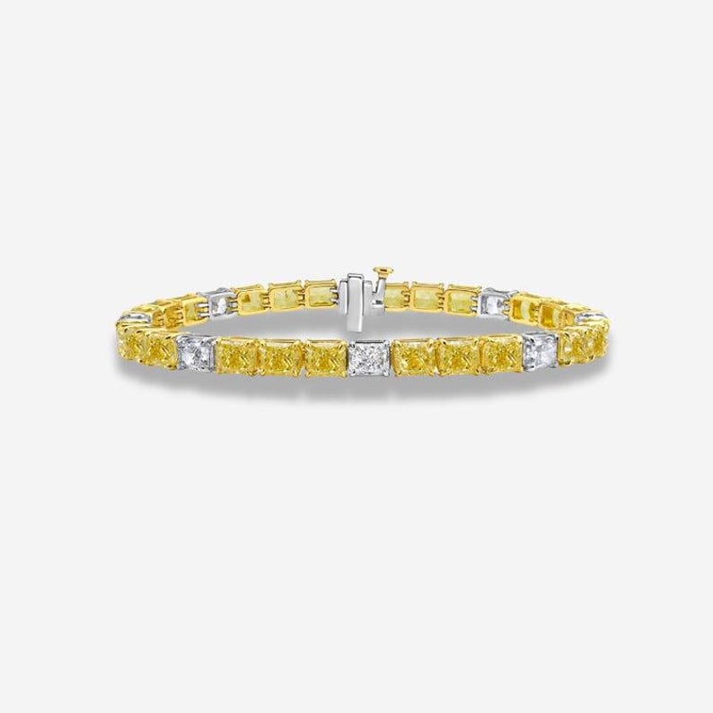 May include: A gold and silver bracelet featuring a series of yellow and white rectangular gemstones. The bracelet has a clasp closure and is displayed against a white background. The gemstones are evenly spaced.