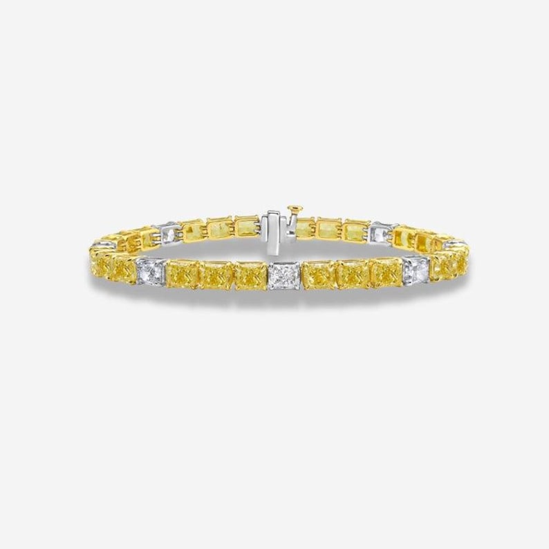 May include: A gold and silver bracelet featuring a series of yellow and white rectangular gemstones. The bracelet is secured with a clasp and is displayed against a white background. The gemstones are evenly spaced.
