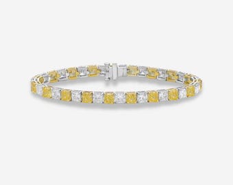 May include: A tennis bracelet featuring alternating yellow and white square-cut gemstones set in a silver and gold band. The bracelet is secured with a silver clasp and is displayed on a white background.