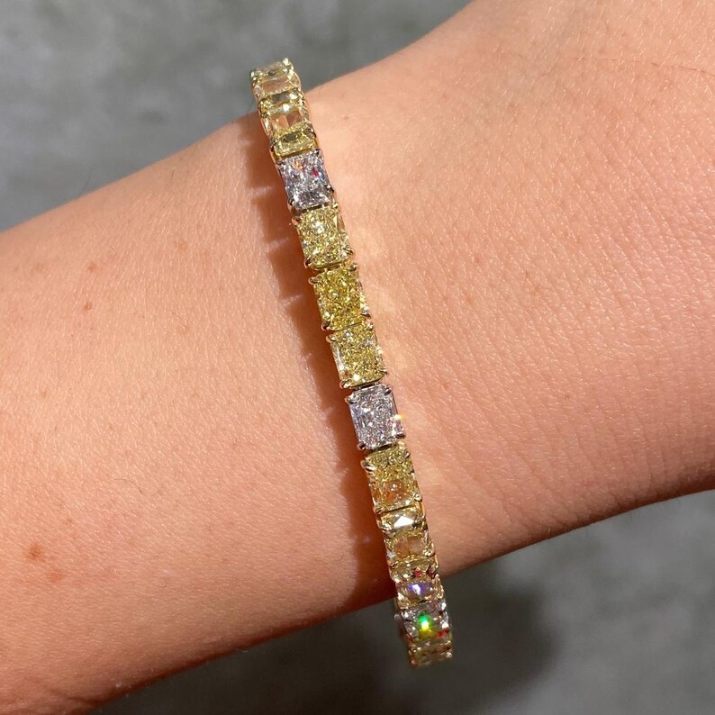May include: A gold bracelet featuring a series of square-cut, yellow and white gemstones. The bracelet is displayed on a person's wrist, showcasing the alternating colors and the sparkle of the gems. The bracelet is a piece of jewelry.