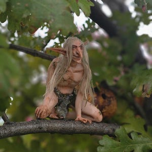 Puede incluir: Una pequeña figura de duende de piel pálida, con cabello largo, liso y claro y orejas puntiagudas, agachada sobre una rama de árbol. La figura tiene una nariz afilada, piel texturizada y viste un taparrabos oscuro y desgarrado. Texto: MidDreamers Bralth.