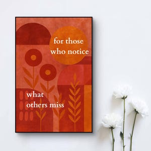 Op de afbeelding: Een ingelijste kunstdruk met een geometrisch ontwerp in tinten rood en oranje. De print bevat de tekst "for those who notice what others miss" in het wit. Het kunstwerk wordt weergegeven tegen een witte muur, met witte bloemen op de voorgrond.