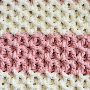 May include: A close-up of a crocheted blanket with alternating stripes of pink and white yarn. The blanket has a textured, open-weave design.