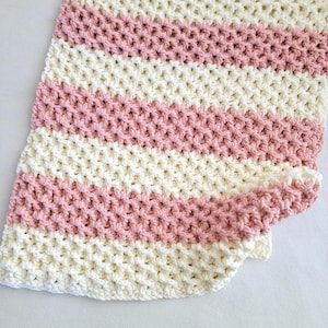 May include: A white and pink crocheted baby blanket with a waffle stitch pattern.