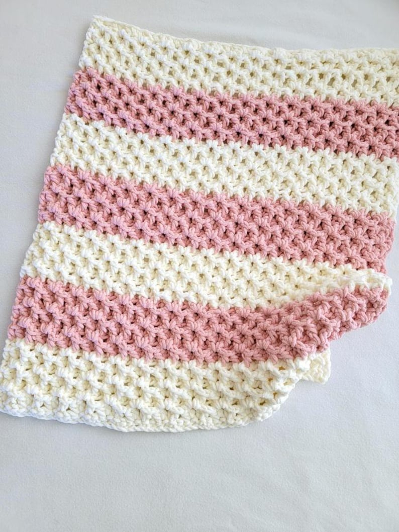 May include: A white and pink crocheted baby blanket with a waffle stitch pattern.