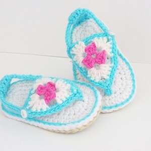 May include: A pair of crocheted baby sandals in white and blue with a pink flower design.