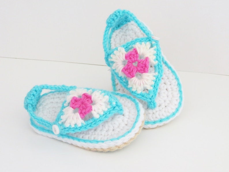 May include: A pair of crocheted baby sandals in white and blue with a pink flower design.