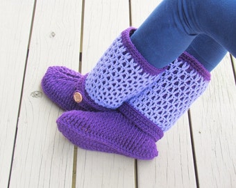 May include: Purple and lavender crocheted slipper boots with a button detail. The boots are worn on a white wooden floor.