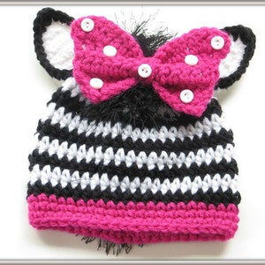 May include: Black and white striped crocheted hat with a pink bow and white polka dots. The hat has black and white ear flaps.