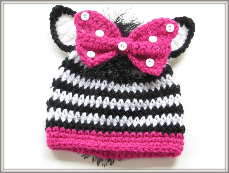 May include: Black and white striped crocheted hat with a pink bow and white polka dots. The hat has black and white ear flaps.