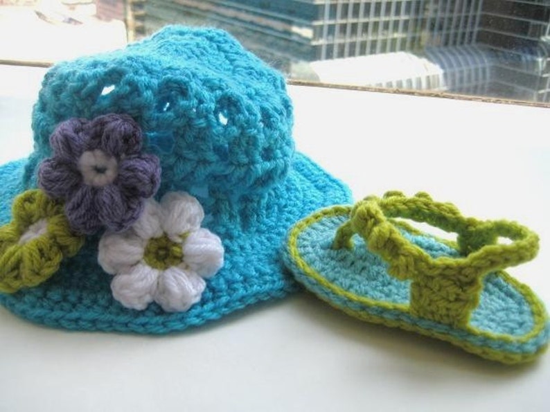 May include: A crocheted blue sun hat with white and purple flowers and a matching pair of green and blue crocheted sandals.