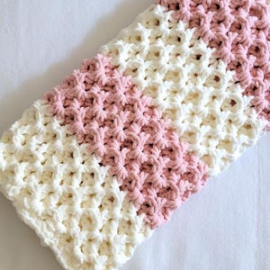 May include: A crocheted baby blanket with a white and pink striped pattern. The blanket is made with a soft, textured yarn.