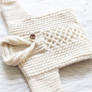 May include: Cream-colored, hand-crocheted baby sweater and hat set. The sweater features a textured stitch pattern, a decorative button closure, and a unique open-weave design on the front. The matching hat has a folded brim, creating a cozy and stylish ensemble.