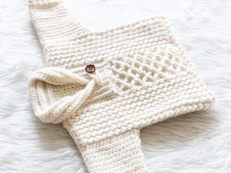 May include: Cream-colored, hand-crocheted baby sweater and hat set. The sweater features a textured stitch pattern, a decorative button closure, and a unique open-weave design on the front. The matching hat has a folded brim, creating a cozy and stylish ensemble.
