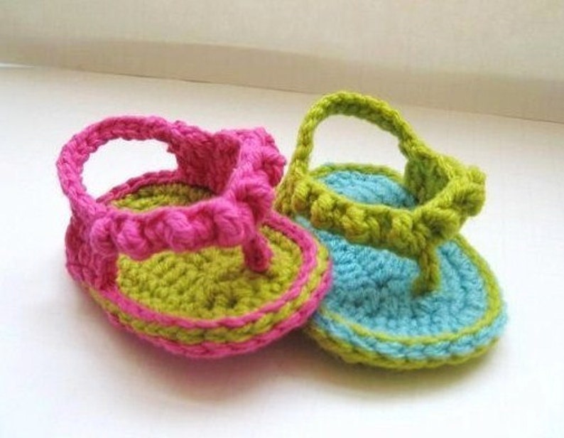 May include: Two pairs of crocheted baby sandals. One pair is pink and green, the other is blue and green.
