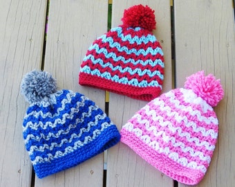 May include: Three crocheted hats with pom-poms in blue, pink, and red with white zig-zag patterns.