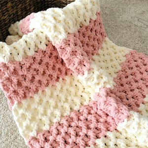 May include: A pink and white striped crocheted blanket with a chunky knit texture.