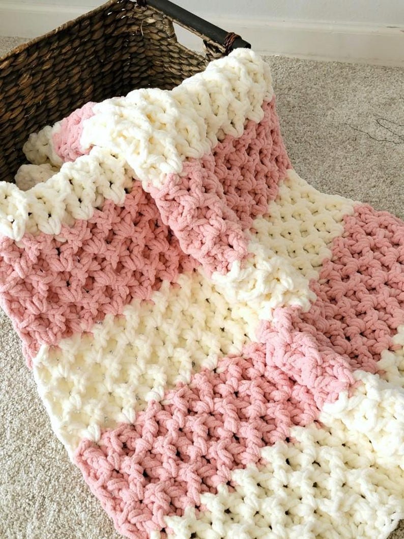 May include: A pink and white striped crocheted blanket with a chunky knit texture.