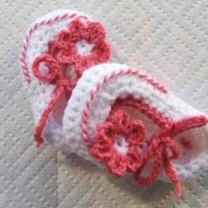 May include: A pair of white crocheted baby booties with pink flower accents and white ribbon ties.