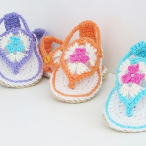 May include: Three pairs of crocheted baby sandals in purple, orange, and blue with white and pink flower accents.