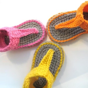 May include: Three pairs of crocheted baby sandals in pink, orange, and yellow. Each sandal has a gray sole and a strap across the top.