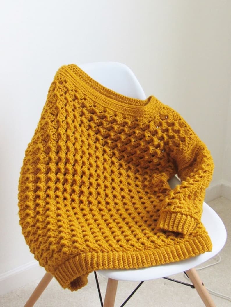 May include: A mustard yellow crocheted sweater with a loose fit and a textured stitch pattern.