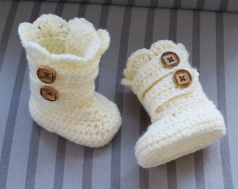 Op de afbeelding: Een paar witte gehaakte babyschoentjes met houten knoopaccenten.