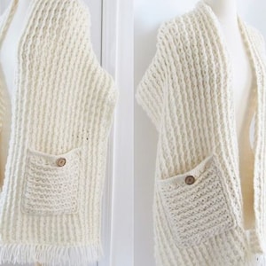 May include: A white crocheted cardigan with two pockets and a button fastening. The cardigan has a fringe trim.