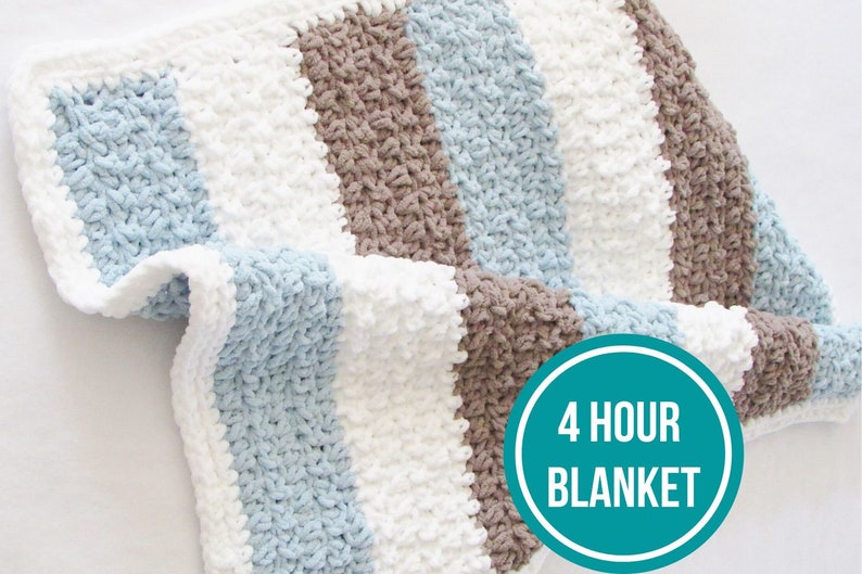 K&ouml;nnte beinhalten: Eine gestreifte H&auml;keldecke in Blau, Wei&szlig; und Braun. Die Decke ist aus einem dicken Garn gefertigt und hat eine strukturierte Optik. Der Text "4 HOUR BLANKET" befindet sich auf einem t&uuml;rkisfarbenen Kreis in der unteren rechten Ecke des Bildes.