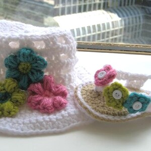 May include: White crocheted sun hat with a pink, green and blue flower embellishment. Matching crocheted sandals with a pink, green and blue flower embellishment.