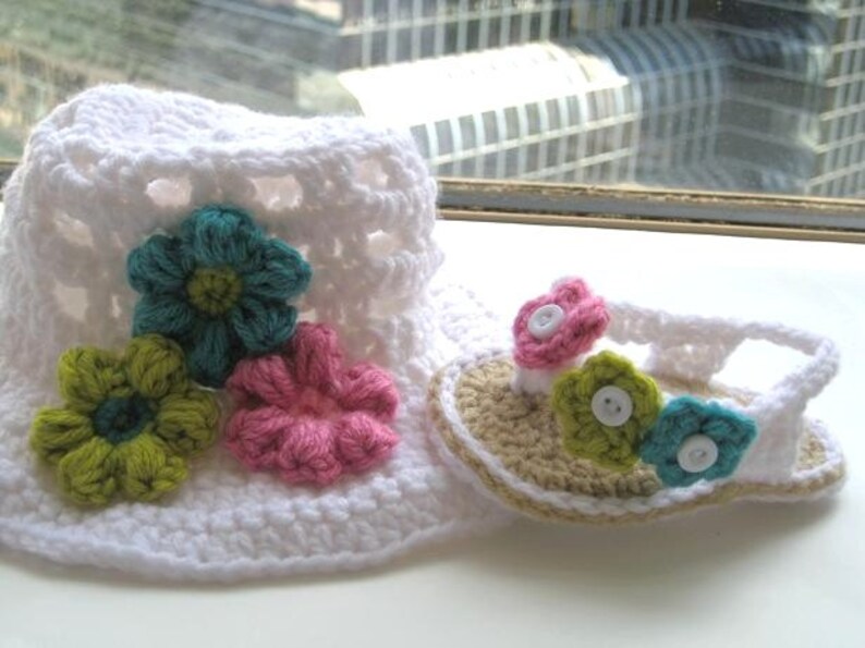 May include: White crocheted sun hat with a pink, green and blue flower embellishment. Matching crocheted sandals with a pink, green and blue flower embellishment.
