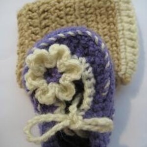 May include: Purple crocheted baby booties with a white flower and a beige crocheted leg warmer.