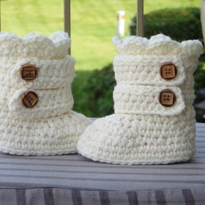 May include: A pair of white crocheted baby booties with brown button accents.