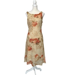 May include: A sleeveless, knee-length dress with a floral pattern. The dress features a cream-colored background with large, peach-colored rose blooms and a subtle, ornate design. The dress is displayed on a white mannequin.