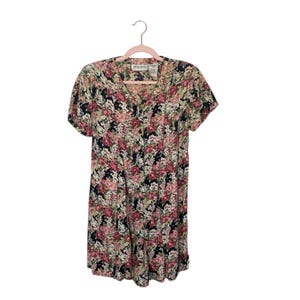 May include: A vintage floral print dress with a V-neck and short sleeves. The dress features a pattern of pink, white, and black flowers on a light background. The dress is hanging on a pink hanger.