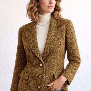 Puede incluir: Una blazer de tweed marrón con botones dorados y dos bolsillos delanteros. La blazer tiene un diseño clásico y se lleva sobre un cuello alto blanco. La chaqueta es una mezcla de hilos marrones, naranjas y amarillos.