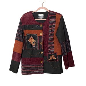 May include: A patchwork jacket with a mix of textures and colors, including burgundy, rust, and black. The jacket features embroidered details and gold-colored buttons. The label reads "Vimmagic".