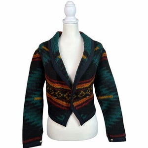 May include: A cropped, long-sleeved cardigan featuring a textured, fuzzy knit with a geometric pattern in shades of black, teal, orange, and yellow. The garment has a shawl collar, a dark trim along the edges, and small metallic buttons at the cuffs.