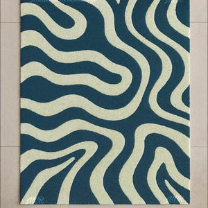 May include: A rectangular rug with a wavy pattern. The rug features a dark blue background with cream-colored, flowing lines. The text "Modern Creation Rugs" and "MCR" are visible.
