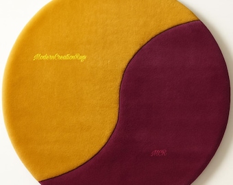 Puede incluir: Alfombra redonda en amarillo mostaza y burdeos. La alfombra presenta un diseño bicolor con una división curva. Los textos "ModernCreationRugs" y "MCR" son visibles en la alfombra.