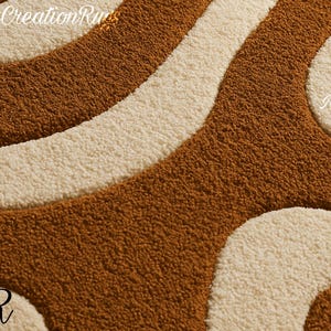 May include: Close-up of a textured rug with a retro design. The rug features a pattern of flowing, curved lines in shades of brown and cream. The letters "MCR" are visible in the corners, and "modernCreationRugs" is at the top.
