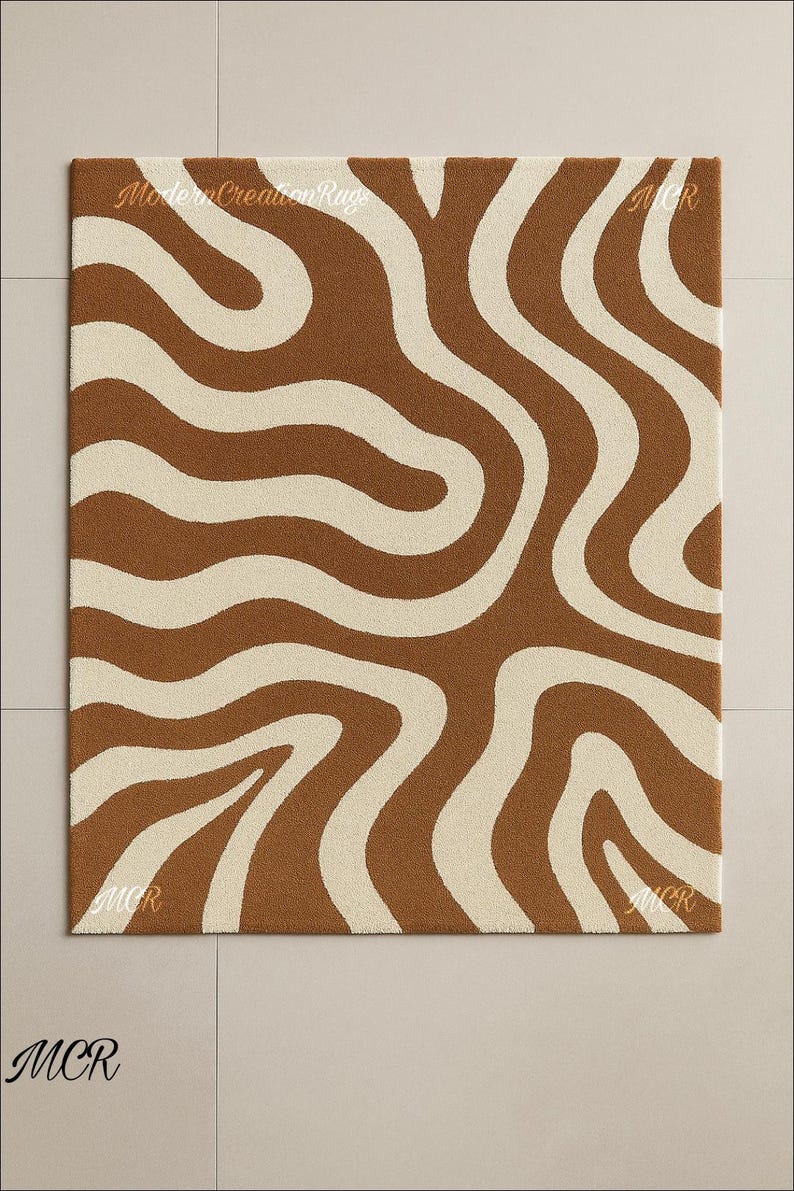 May include: Brown and cream-colored rug with a wavy pattern. The rug has a square shape and features a repeating design of flowing, organic lines. The text "Modern Creation Rugs" is visible on the top of the rug. The letters "MCR" are visible in the corners.