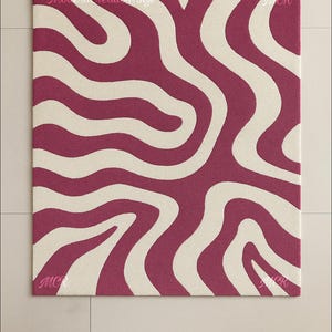 May include: A rectangular rug with a bold, abstract design. The rug features a pattern of flowing, wavy lines in a deep magenta color against a cream-colored background. The text "Modern Creation Rugs" is visible. The rug is a decorative floor covering.