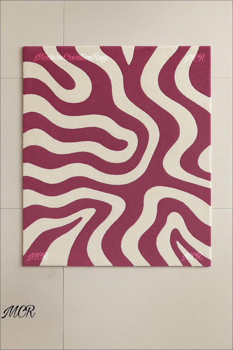 May include: A rectangular rug with a bold, abstract design. The rug features a pattern of flowing, wavy lines in a deep magenta color against a cream-colored background. The text "Modern Creation Rugs" is visible. The rug is a decorative floor covering.