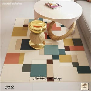 Könnte beinhalten: Geometrischer Teppich mit cremefarbenem Hintergrund und bunten Quadraten in Türkis, Koralle, Gold und Braun. Ein goldfarbener Hocker und ein weißer Tisch mit Holzbein befinden sich auf dem Teppich. Der Teppich hat den Text "ModernCreationRugs".