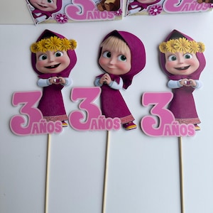 Pode incluir: Tr&ecirc;s topos de bolo com uma menina de desenho animado em um vestido e capuz roxos, com uma coroa de flores amarelas. Cada topo tem o n&uacute;mero 3 rosa e a palavra "A&ntilde;os". Os topos est&atilde;o em palitos de madeira.