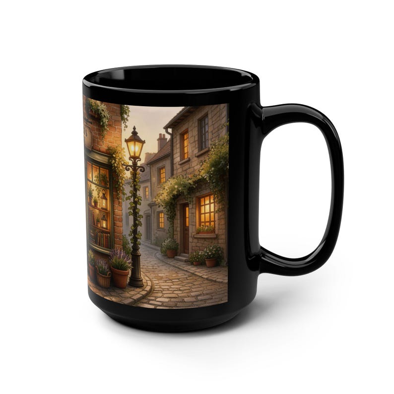 May include: Black ceramic mug with a charming street scene print. The image shows a cobbled street, old buildings, and a vintage lamppost, evoking a quaint European village. The artwork features warm lighting from windows and street lamps. Ideal for tea or coffee.