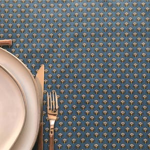May include: A blue placemat with a repeating pattern of yellow and white floral designs. A white plate, a fork, and a knife are on the placemat, suggesting a dining setting.