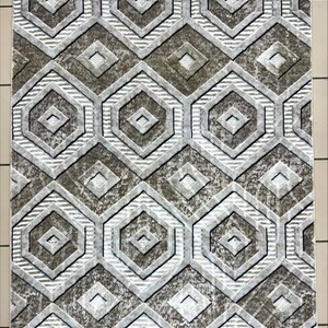 Peut inclure: Un tapis rectangulaire avec un motif géométrique. Le design présente des hexagones et des losanges répétés dans des tons de gris, de marron et de blanc. Le tapis a un aspect texturé, avec des éléments en relief créant de la profondeur et un intérêt visuel. Le style général est moderne.