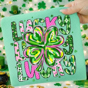 Puede incluir: Un artículo cuadrado de color verde claro con las palabras "LUCKY LUCKY" en una mezcla de patrones y colores. El diseño incluye un gran trébol de cuatro hojas en verde, rosa y amarillo. Las letras están decoradas con tréboles y otros motivos del Día de San Patricio.
